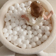 Peuter speelt in een crèmewitte bouclé schildpad-ballenbak op een vloerkleed