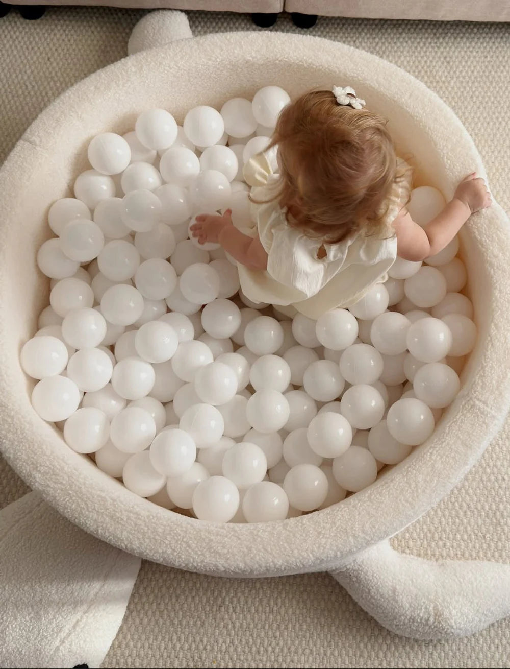 Peuter speelt in een crèmewitte bouclé schildpad-ballenbak op een vloerkleed