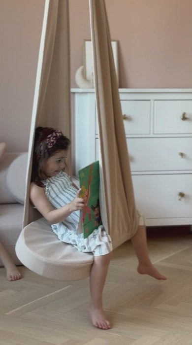 Meisje leest boek in hangstoel, lichte kamer met witte ladekast.