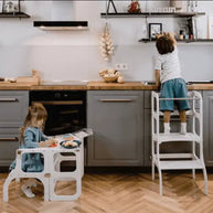 Kinderen gebruiken de Houten Learning Tower 2in1 - wit in de keuken voor veilige activiteiten.