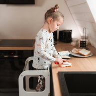 Kind staat veilig op Houten Learning Tower 2in1 - wit en smeert brood in keuken