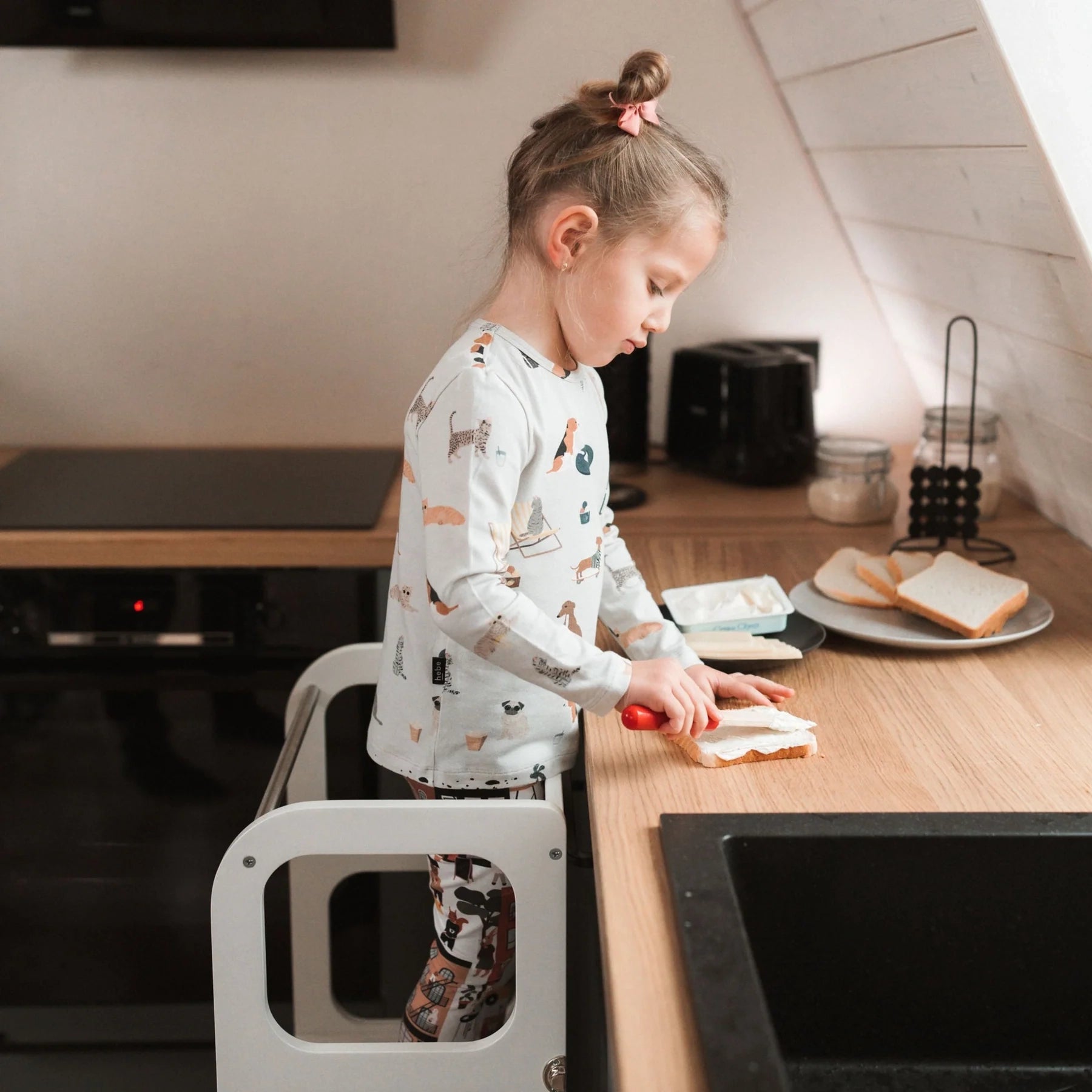 Kind staat veilig op Houten Learning Tower 2in1 - wit en smeert brood in keuken