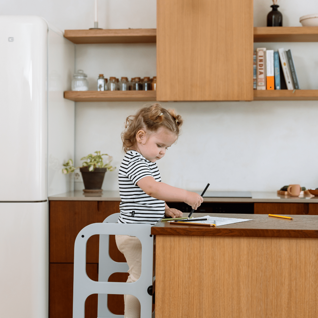 Kind tekent zittend op Houten Learning Tower 2in1 wit in moderne keuken