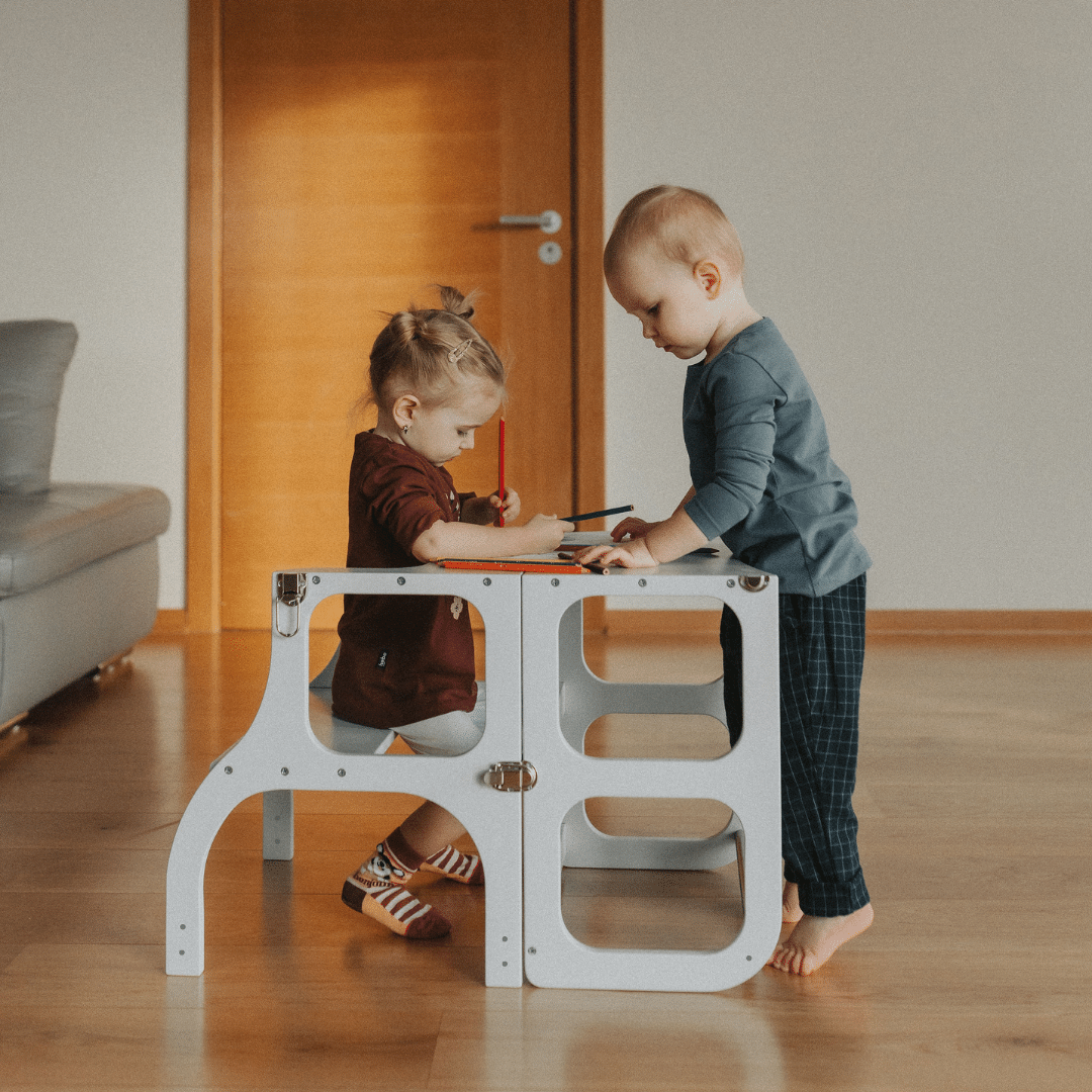 Twee kinderen spelen aan de Houten Learning Tower 2in1 - wit in een woonkamer