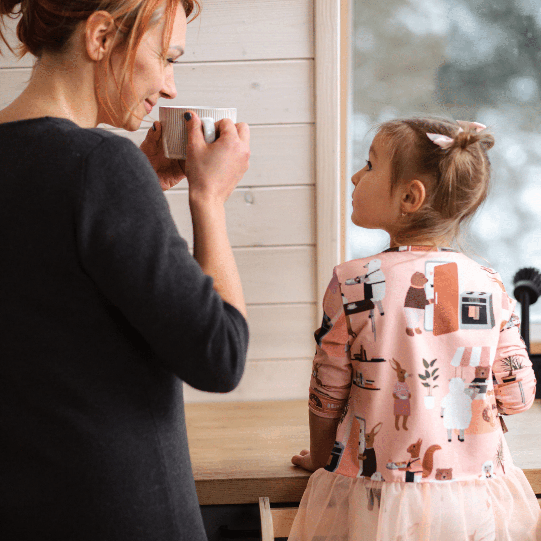 Moeder en kind in de keuken met Houten Learning Tower 2in1 - wit zichtbaar naast het raam