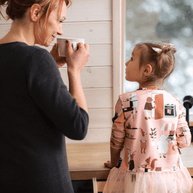 Moeder en kind in de keuken met Houten Learning Tower 2in1 - wit zichtbaar naast het raam