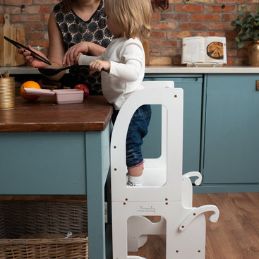 Kind staat op de Houten Learning Tower - Wit in de keuken bij tafel met moeder