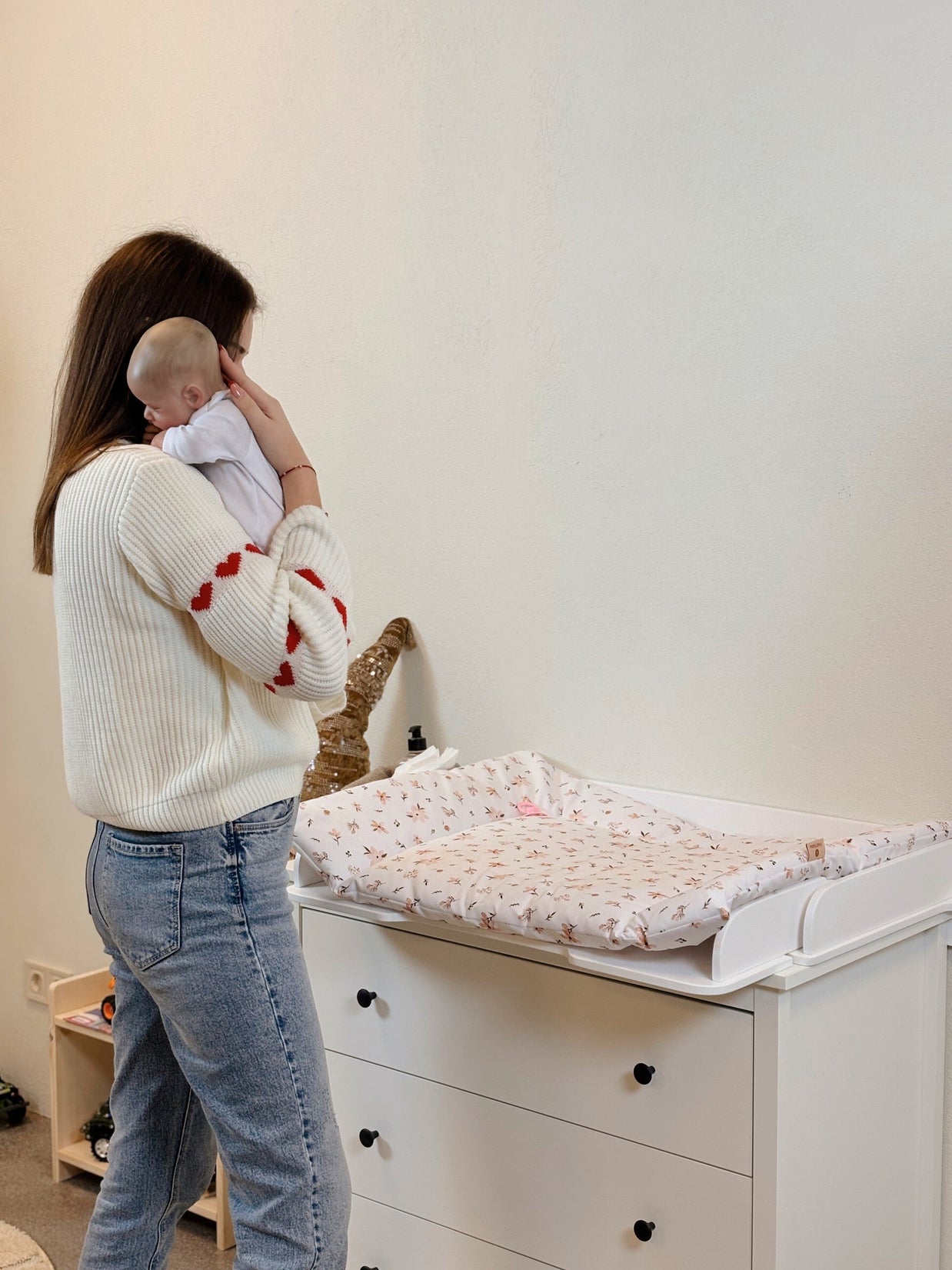 Moeder houdt baby vast naast commode met Family-scl Verschoonmat in neutrale kamer