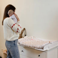 Moeder houdt baby vast naast commode met Family-scl Verschoonmat in neutrale kamer