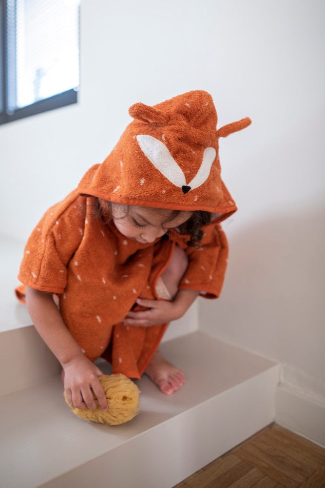 Kind in oranje vossenbadponcho zit op witte trap met een spons.