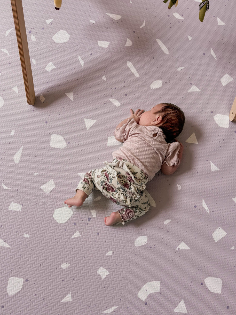 Baby ligt op zachte Olya Kids Puzzel Speelmat Terrrazo Lavender met lavendelpatroon