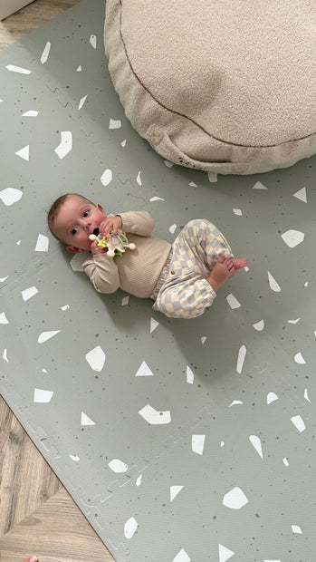 Baby ligt op zachte Olya Kids Puzzel Speelmat Terrazzo Sage met stijlvol patroon