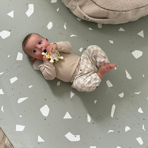 Baby ligt op zachte Olya Kids Puzzel Speelmat Terrazzo Sage met stijlvol patroon