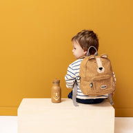 Kind met rugzak en Drinkfles Mr Bear - 350 ml op een lichte houten bank tegen oker muur
