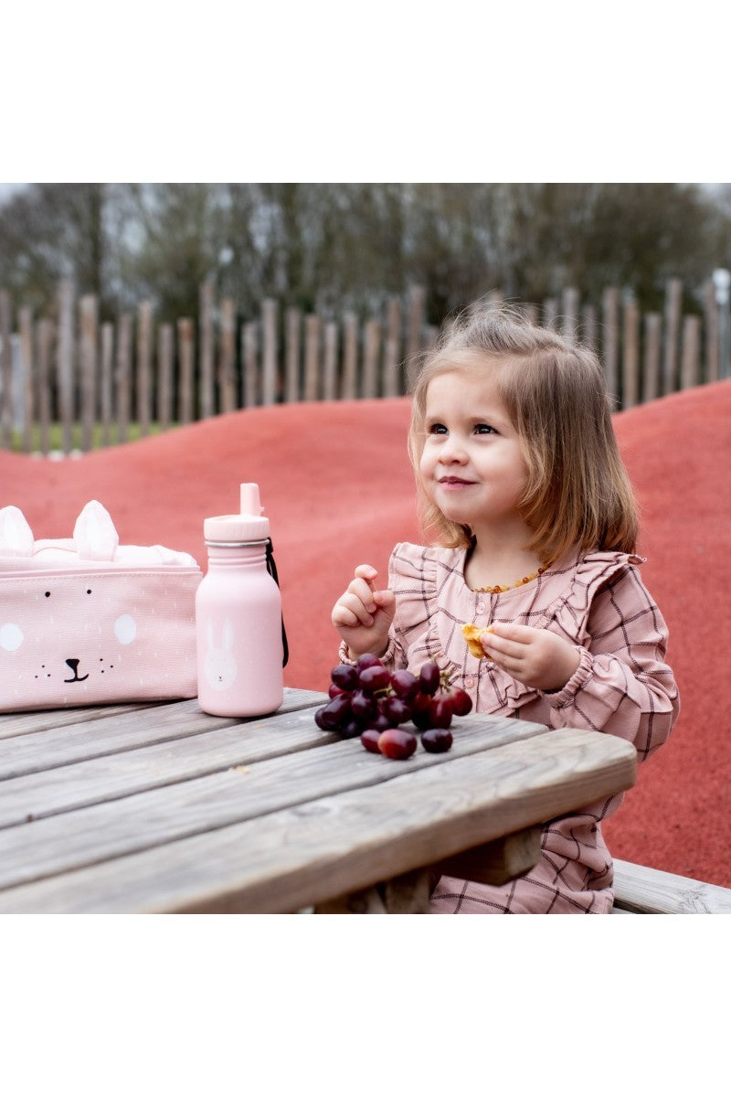 Meisje zit buiten met Trixie Drinkfles Mrs. Bunny 350 ml en fruit op houten tafel