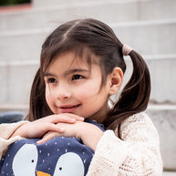 Meisje met paardenstaarten knuffelt vrolijk haar Trixie Schooltas Mr Penguin rugzak