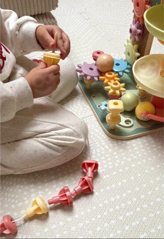 Kind speelt met Houten Activiteitenboom 4 in 1 - Knikkerbaan, Vormenstoof, Tandwiel en Kralenlabyrint