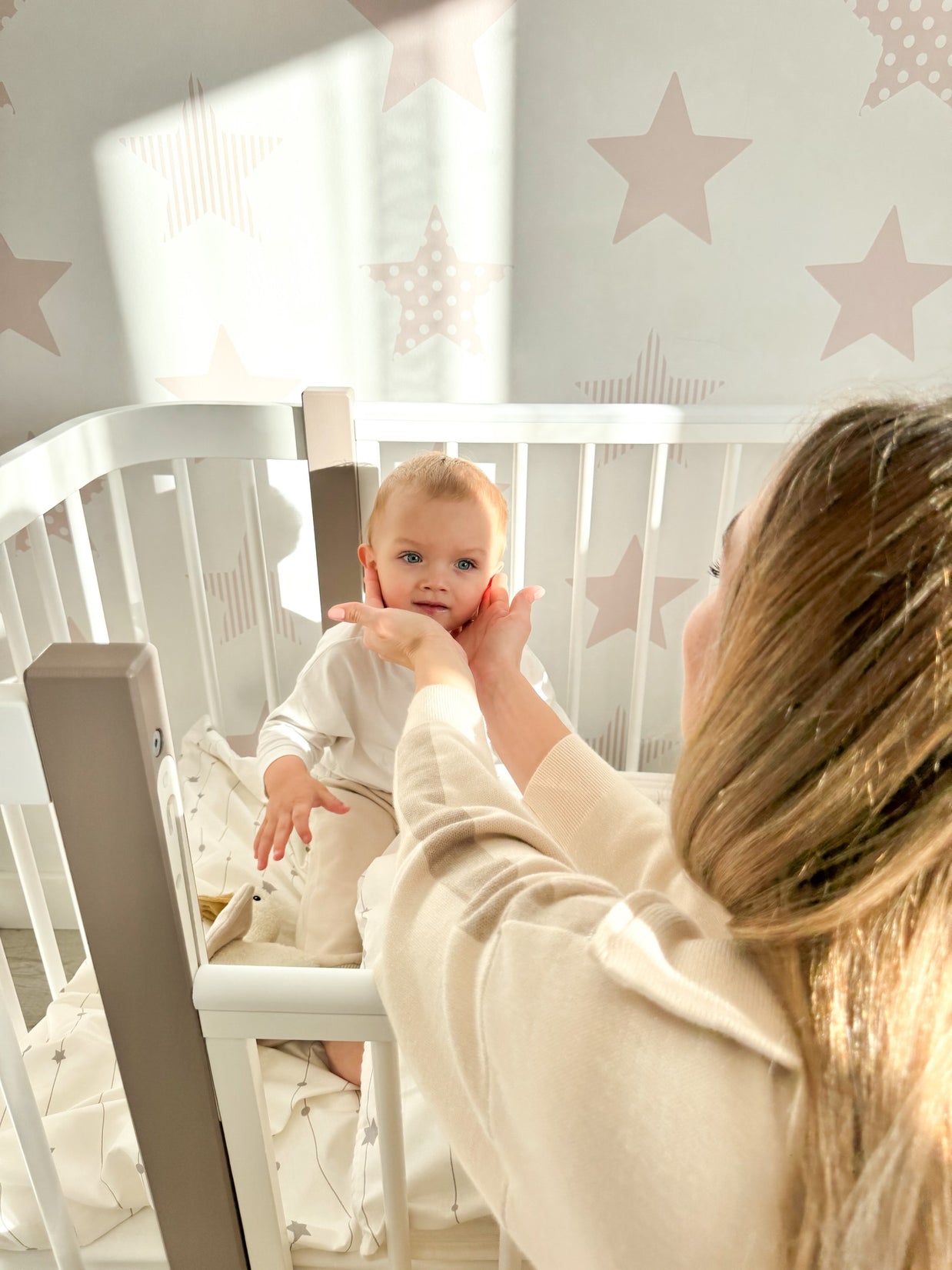 Moeder aait haar baby die in het cappuccino-witte ELIN babybedje zit