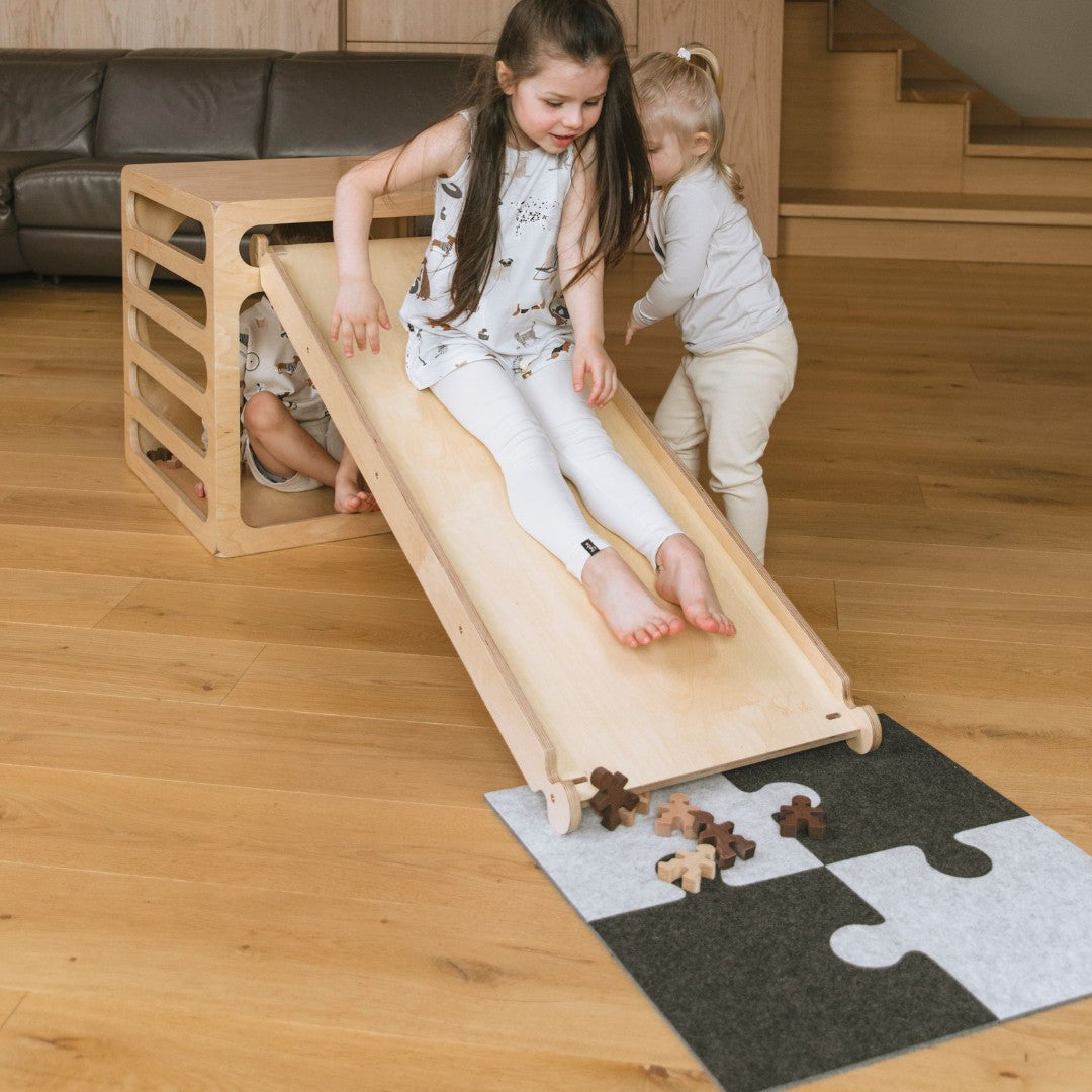 Meisje glijdt van de glijplank met de vilten puzzel-speelmat eronder
