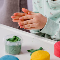 Kinderhandjes rollen biologische klei met potjes groene, blauwe en gele klei ernaast