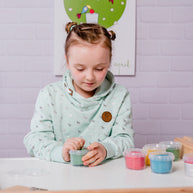 Meisje aan tafel speelt met de potjes kleurige biologische klei