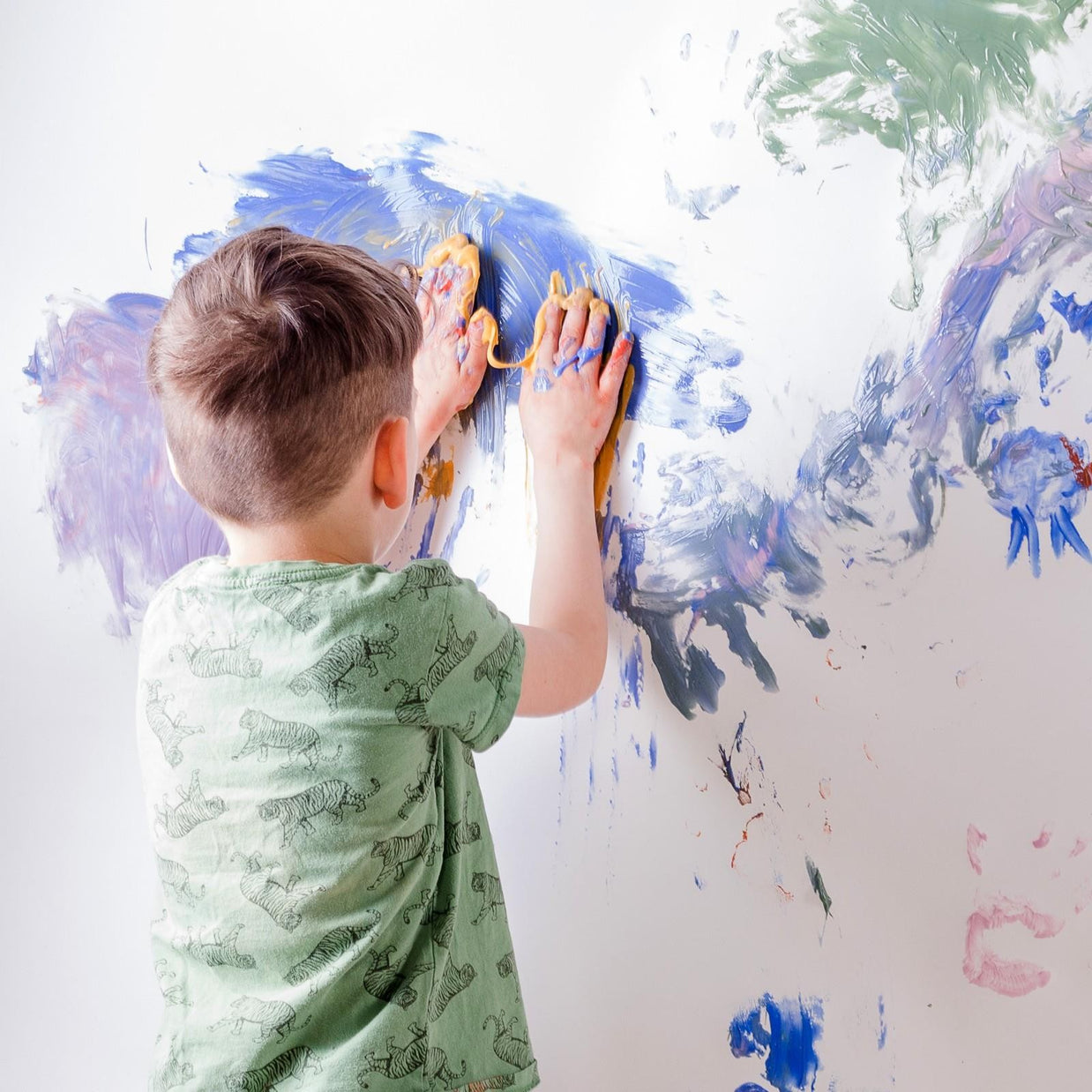 Kindje smeert met blauwe en gele biologische vingerverf op de muur