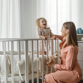 Moeder en peuter bij het witte ovale babybed OLIN in de babykamer