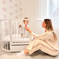 Moeder en baby spelen bij het ovale babybed OLIN met sterrenbehang
