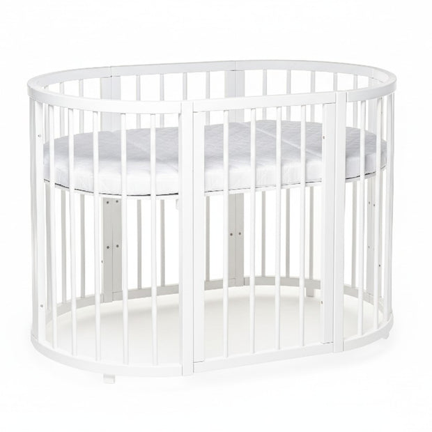 Lachende baby ligt op de matras van het ovale babybed OLIN, bovenaanzicht