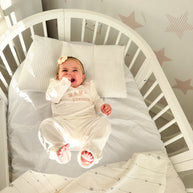 Lachende baby ligt in het ovale babybed OLIN, bovenaanzicht