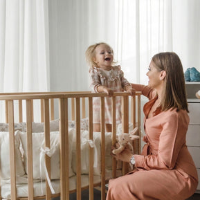 Moeder en lachende peuter bij het houten babyledikant Olin in een lichte babykamer