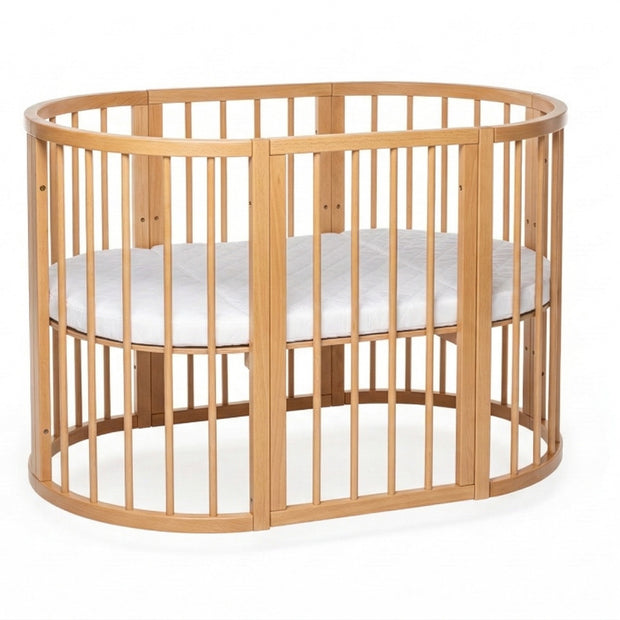 Ovaal houten babyledikant Olin in natural met witte matras op studioachtergrond