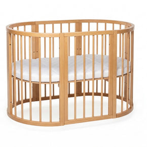 Ovaal houten babyledikant Olin in natural met witte matras op studioachtergrond