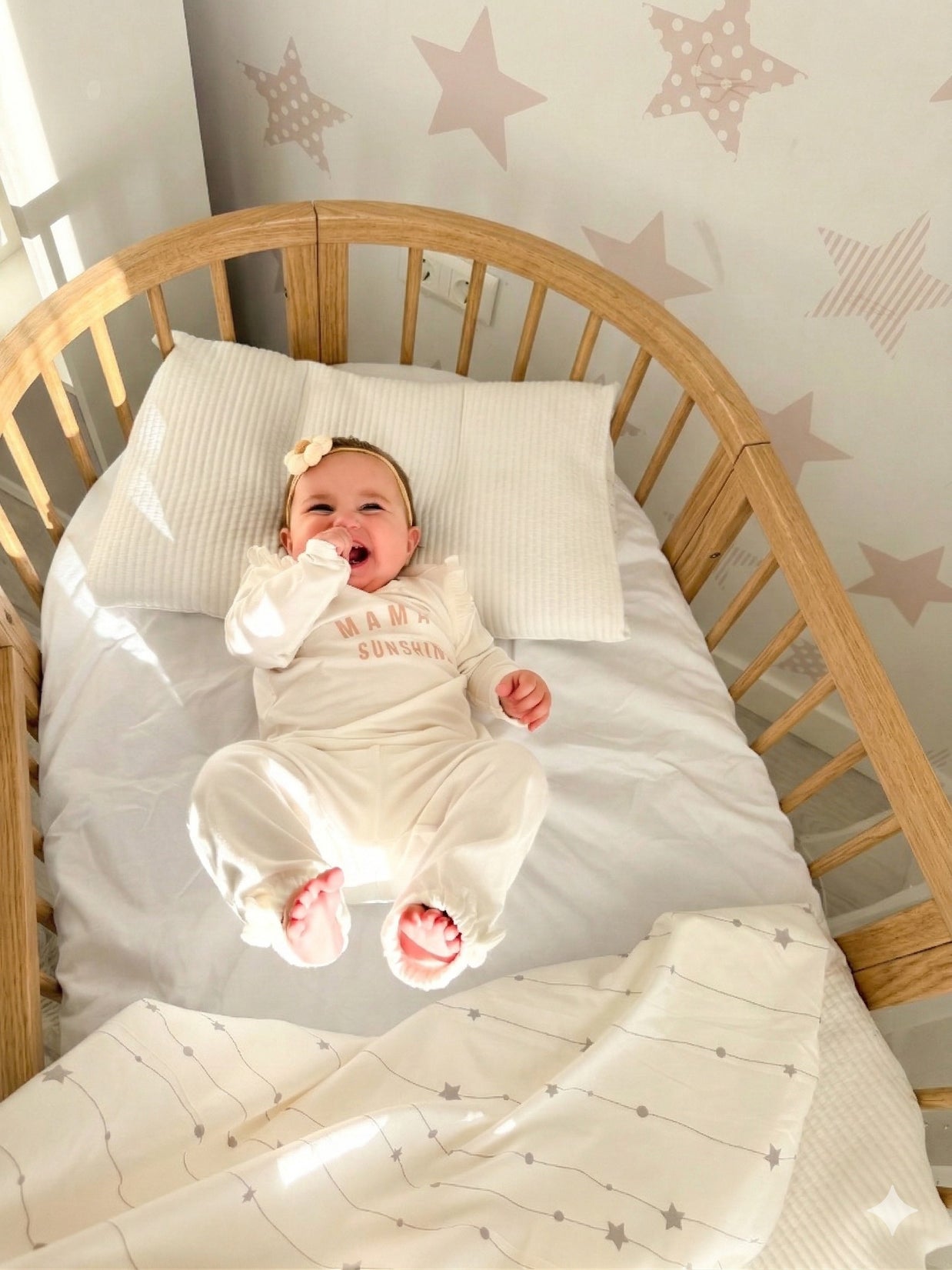 Lachende baby in het houten babyledikant Olin tegen een wand met sterretjes