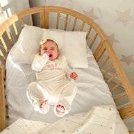 Lachende baby in het houten babyledikant Olin tegen een wand met sterretjes