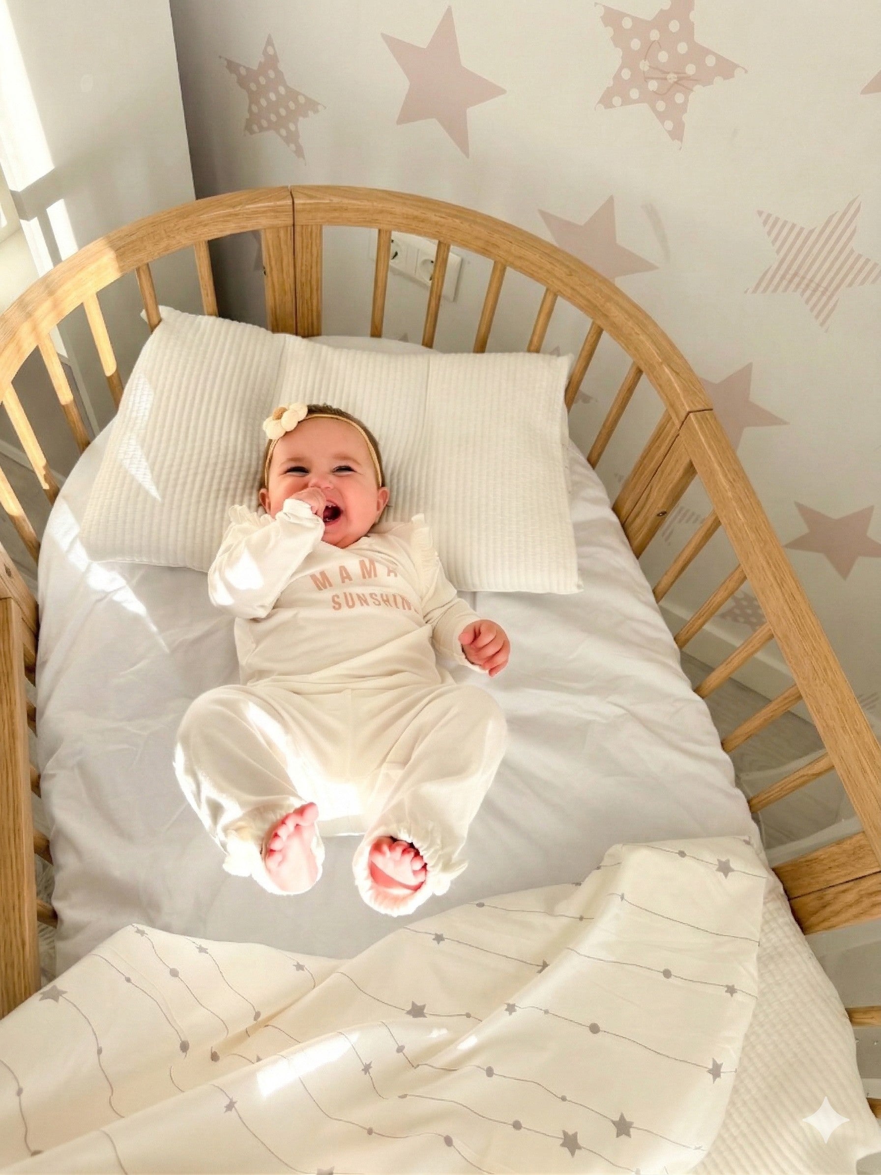 Lachende baby in het houten babyledikant Olin tegen een wand met sterretjes