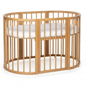 Ovaal houten babyledikant Olin in natural met witte matras van opzij