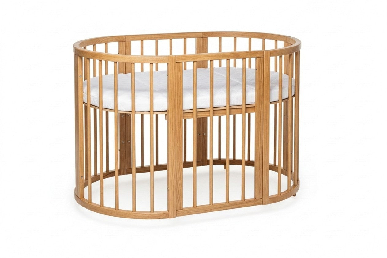 Ovaal houten babyledikant Olin in natural met witte matras van opzij