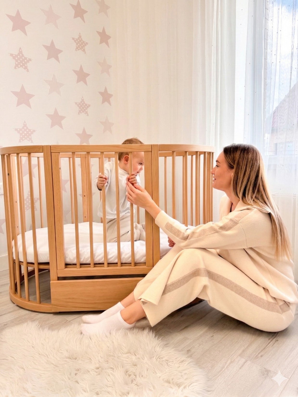 Moeder en baby spelen samen bij het houten babyledikant Olin in de kinderkamer