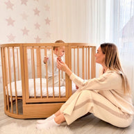 Moeder en baby spelen samen bij het houten babyledikant Olin in de kinderkamer